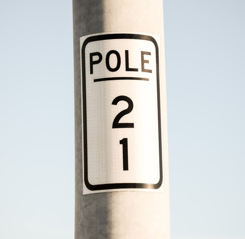 A close up of a pole near the walkway of the Arthur Ravenel bridge in Charleston SC.  There is a sticker on the pole that says "Pole 21" with the "21" running vertically.  