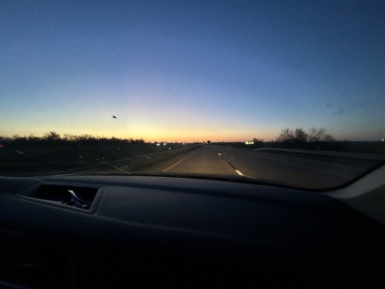 Twilight sky over a highway captured from inside a car, with oncoming traffic and a clear view of the road ahead.