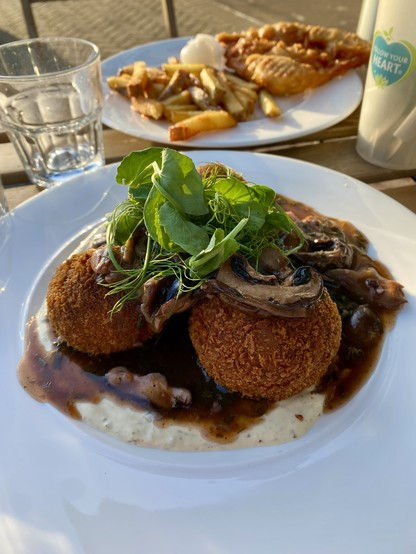 Plated on a sunny restaurant patio: Haggis & rooster mash potato cakes coated with panko breadcrumbs and deep fried until crispy. Served on chestnut mushroom ragout & green peppercorn yogurt 