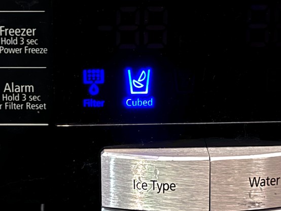Close-up of a refrigerator’s ice type selector. A blue-backlit icon states it will dispense “cubed” ice as opposed to crushed, however the shape of ice depicted is not cubes, rather the variety that is flat on one side and curved on the other—a cursed shape that frequently dams up the beverage in a cup, resulting in the all-too-familiar gush of liquid when the cup is tipped back too far while trying to actually take a drink.