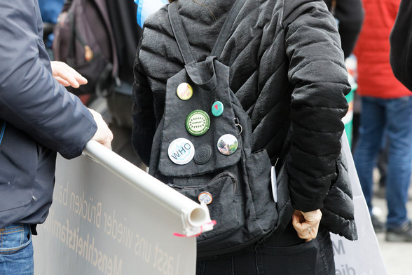 Zu sehen ist ein Rucksack mit verschiedenen Stickern. Auf einem steht „Stoppt den WHO Pandemievertrag“.