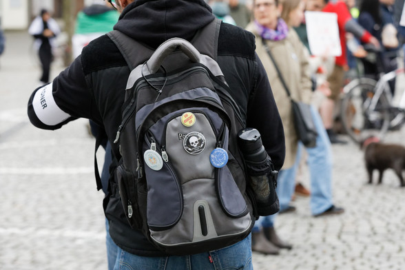 Zu sehen ist ein Rucksack mit verschiedenen Stickern. Auf einem steht „Mensch zweiter Klasse – gesund und ungeimpft“.