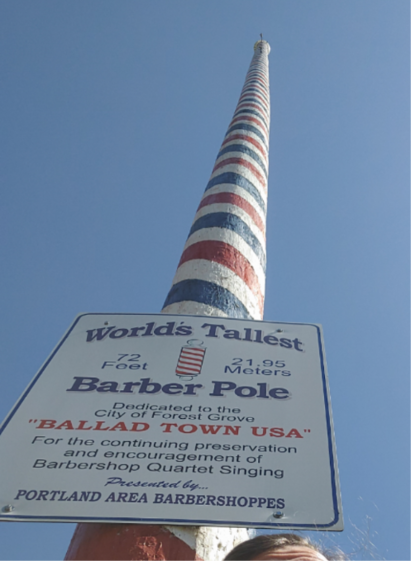 A very tall pole painted with red white and blue stripes. The sign reads "world's tallest barber pole 72 ft to 21.95 m dedicated to the city of Forest Grove "BALLAD TOWN USA" for the continuing preservation and encouragement of barbershop quartet singing presented by Portland Area Barbershoppes"