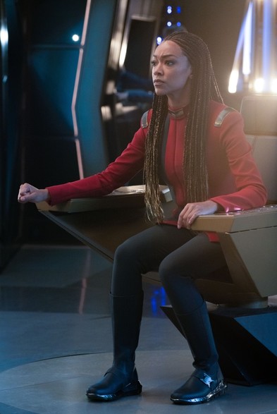 Capt Burnham (Sonequa Martin-Green) sits leaning forward attentively in the Captain’s Chair of the U.S.S. Discovery.