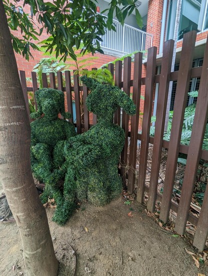 A wooden fence. 
Two seated figures, made of topiary. They are humanoid with dog and rabbit heads