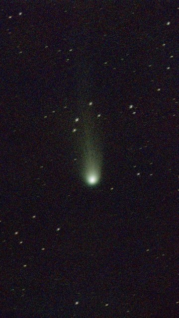 A green-ish comet with a bright nucleus and fuzzy coma surrounded by stars against the backdrop of space.