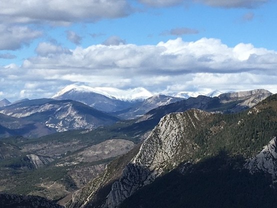 snow covered mountain range in the background surrounded by other mountains in various shades of gray and green (where populated by spruce)