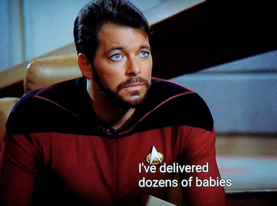 TNG scene. Commander Riker, in red uniform, is sitting forward on one of the bridge chairs next to the captain's seat. He's looking up and he's laser focused. Closed caption reads, "I've delivered dozens of babies"