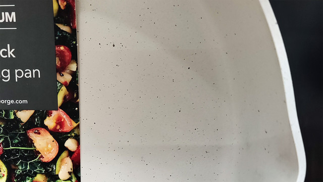 Cropped photo of a frying in a supermarket. The pan has a light cream colour coating, with tiny black flecks, making it look dirty. 