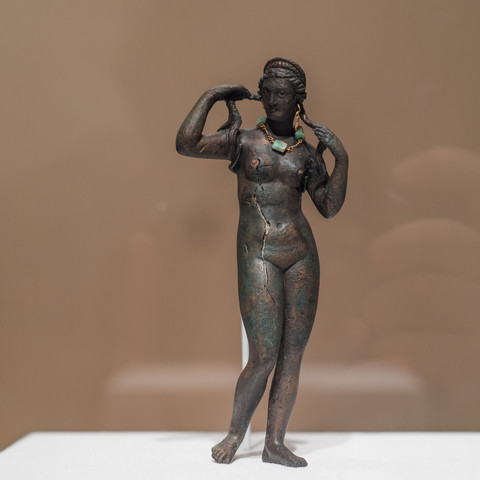 Statuette of Aphrodite Anadyomene, Aphrodite rising from the Sea. She is in the nude, wringing out her wet hair. The statuette was cast in bronze with copper used for the nipples. She wears golden earrings and a golden necklace with emeralds.