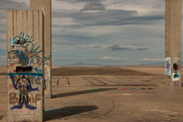 graffiti on a concrete pillar shows a human figure, before a huge expanse of brown and yellow fields and distant mountains