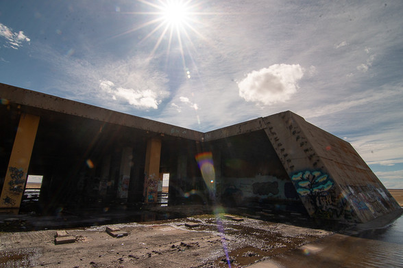 a concrete structure stands in disrepair, under a bright sun shedding rays that refract into rainbow colors, like the graffiti covered concrete pillars.