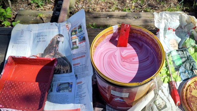 Ein Topf mit Farbe. Noch nicht ganz das gewünschte Rot. Daneben Zeitungen und Malutensilien.