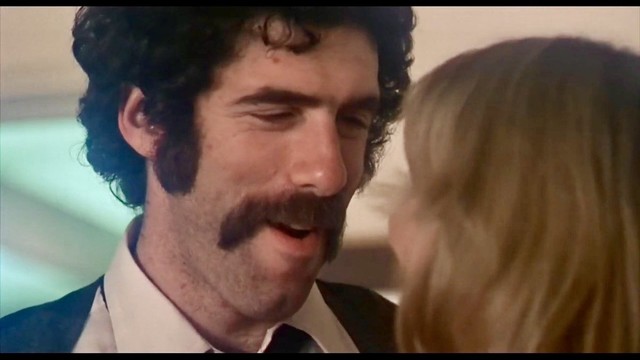 A picture of Elliot Gould in the movie “Busting” (1974). He has full curly hair and magnificent sideburns. In addition, he wears a mustache often called “horseshoe mustache”.