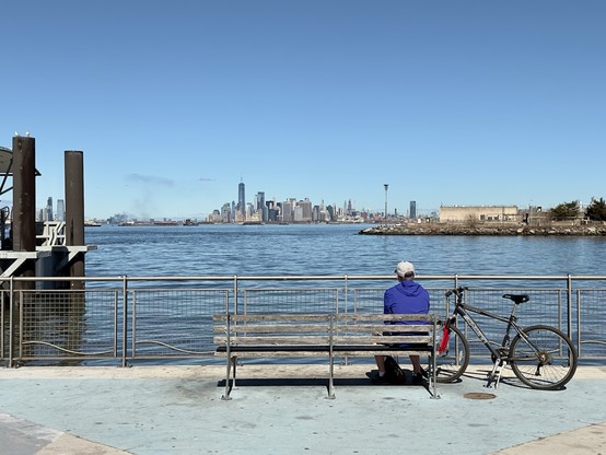 Man on a bench looking over New York Harbor towards Manhattan 