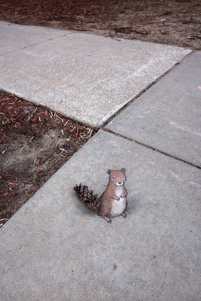 Streetart, auf den Boden gemalt.
Ein Eichhörnchen sitzt scheinbar aufrecht auf der Steinplatte und ein Fichtenzapfen dient als Schwanz.