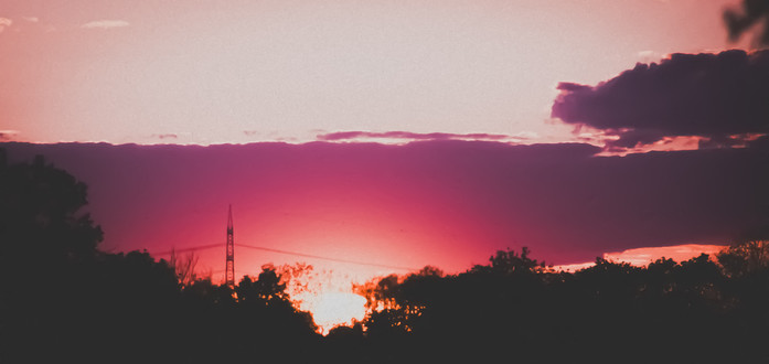 The image captures a serene and picturesque sunset.

Image format: Landscape

Genre: Nature/Scenic Photography

Background: The background is dominated by the setting sun that paints the sky in vibrant hues of pink, purple, and orange. Silhouettes of trees and a transmission tower are visible against the colorful sky.

Colors: The colors transition from a deep purple at the top, becoming progressively lighter with shades of pink and finally culminating into a bright orange at the horizon.