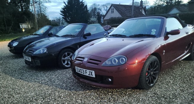 A black MGF, black MG TF and red MG TF sports car parked on a gravel village pub car park.
