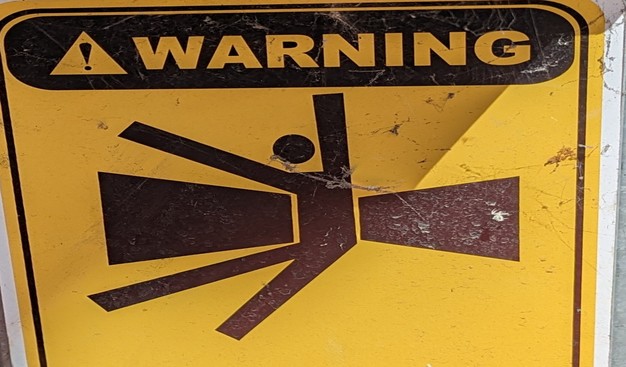 Yellow warning sign
Text just reads "warning".
Graphic shows a stylised person, send up, legs forward, being sucked in/crushed by two black rectangles
