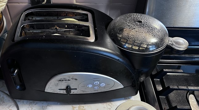 Picture of a black plastic and stainless steel breakfast making toaster with two slice opening and a compartment on the right that is clouded with condensation as it steams an egg and a couple links of sausage.