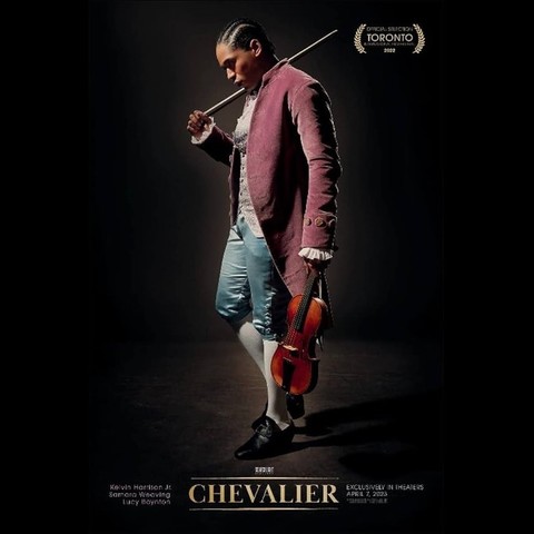 Affiche du film Chevalier. L'acteur du film, un homme noir métisse de profil avec des cheveux cornrows en costume d'époque Louis XVI tient dans sa main gauche, face à nous son violon et dans sa main droite son archet, porté presque comme un fusil. C'est le chevalier Saint George. L'homme regarde vers le bas et derrière lui, une scène de spectacle, complètement vide, noire, sombre et nue. 