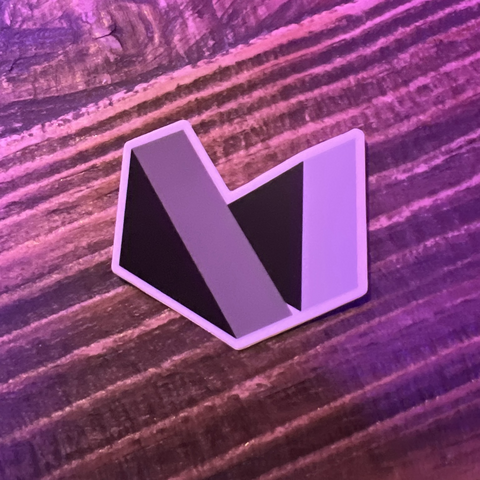 Photo of the Material for MkDocs theme logo as a 2 inch die-cut sticker laying on a wood grain table with warm purple-tinted bar lighting