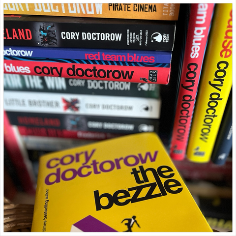 Cory Doctorows The Bezzle in front of a collection of his precious books. 