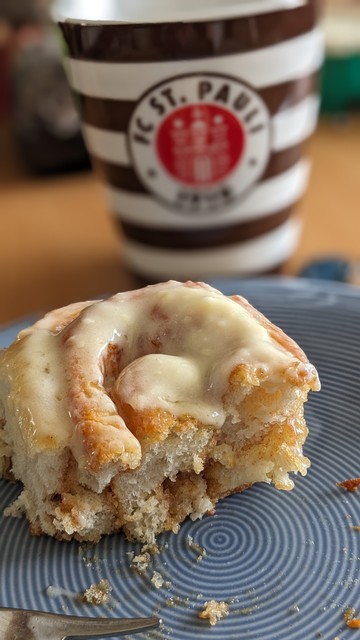 Auf einem Teller liegt eine angefangene Zimtschnecke im Hintergrund eine Tasse von St. Pauli.