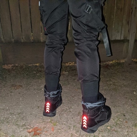 Red vertical lights on the heels of black boots. The lights are designed to look like an upwards-pointing stack of chevrons.