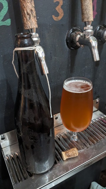 A 750ml champagne style bottle stands on a beer faucet drain next to a goblet glass holding beer that formerly lived in the afore mentioned bottles. The beer is light copper colored with very little head. It tastes of sweet oak and vinegar, a flavor not completely off putting, which makes it difficult to dump out for something better.