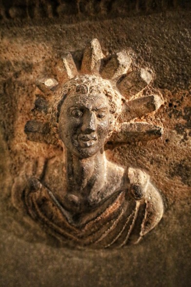 Bust relief of the sun god Helios depicting him with a chiton pinned over both shoulders, full lips and short, curly hair adorned by a nine-spiked sunray crown.