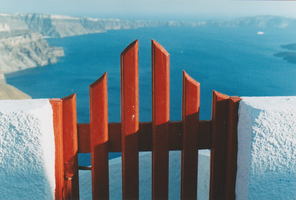 Red wooden gate against a turquoise sea, white painted walls.
