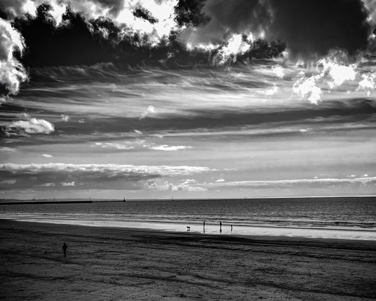 High contrast, black and white photo of the beach with distant figures near the sea.