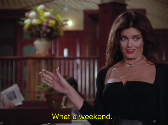Screenshot from Lois & Clark season 1, where the character Cat is raising her right arm saying "What a weekend" (subtitles). She is wearing a black dress with red lipstick and a French manicure.