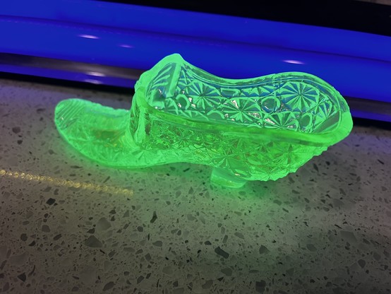 A glowing green glass slipper under blue light.