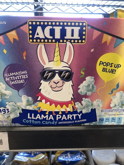 a box of ACT II Llama Party cotton candy-flavored popcorn which “Pops up blue!” and contains ”#llamazing activities inside!” the llama illustration front and center sports two necklaces, sunglasses, and has a horn like a unicorn.