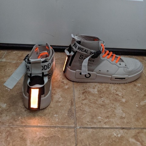 Vertical rectangular lights on the heels of a pair of high tops. High tops are gray with orange laces. The light is of an orange color.