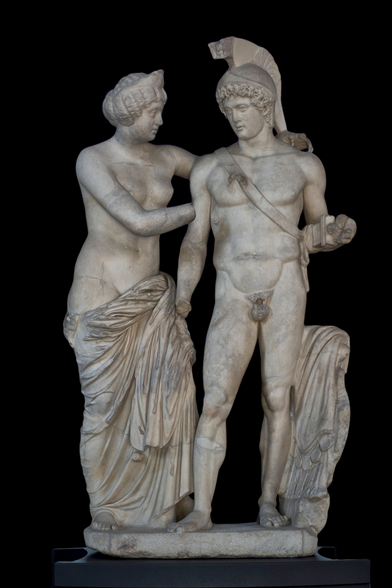 Marble sculpture group of Mars and Venus. The god of war stands on the right, his sword girded around his shoulder, the crested helmet the only item of clothing on his body. Venus stands to his left, her arms wrapped around him. She wears a slipping himation draped around her hips and a crown adorns her hair.