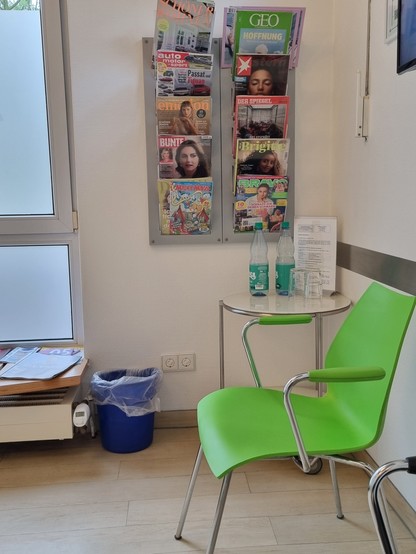 In der Ecke eines Wartezimmers steht ein Stuhl, dahinter an der Wand hängt ein Zeitschriftenhalter mit zehn aktuellen Zeitschriften von Bravo bis Brigitte.