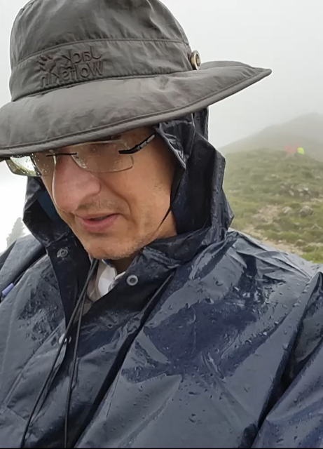 Me walking in the rain on top of a mountain. Wearing a hat and a poncho