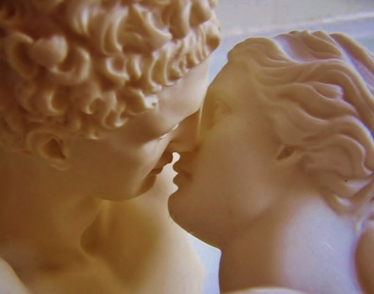 Jasper on Flickr made their copies of a Hermes statue and an Aphrodite statue kiss. Close-up photograph of their faces.