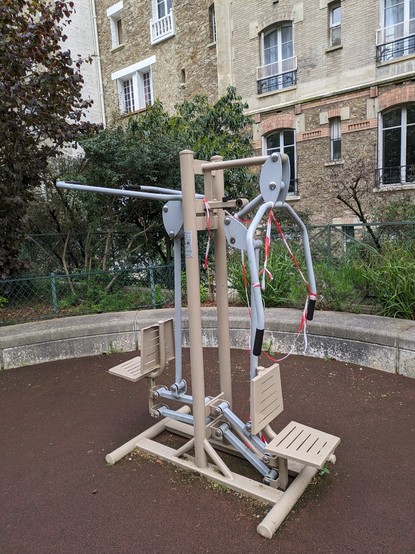 Photo d'un appareil de musculation en plein air dans un parc. La partie droite de la machine est ornée de rubalise rouge et blanche
