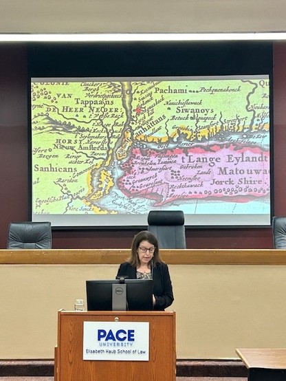 Me (a white woman with brown hair and glasses, wearing a black jacket) showing a 1680s Dutch map of the New York area with the names of the Indigenous Groups that live in each area.  The star, in Weckquaeskeck land, represents White Plains.
