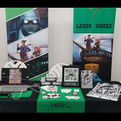 a image of Lasso Games con set up at Eeagle con. A computer on the left is displaying Highway Rampage, Random Quest is displayed in the center, and on the right there is a Random Quest gaming mat. In the background you can see the Lasso Game con banners. 