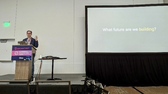 Short of me at a lectern presenting with a slide behind me reading “what future are we building?” Photo credit: Jory Burson