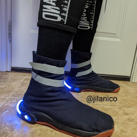 Jika tabi boots of a navy color with gray tanker straps around the ankles. A horizontal strip illuminated by blue LED light wraps around the heel.