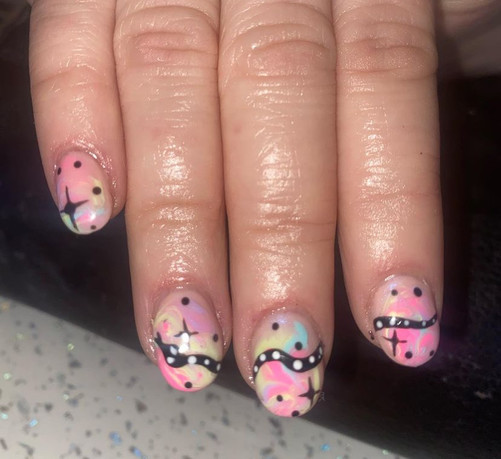 Background is pastel, pink, blue, green, purple and yellow, swirled together. On the middle three fingers, is a black snake with white spots tail on index finger, main body on middle finger and head on ring finger. There are black spots and sparkles dotted around all nails.