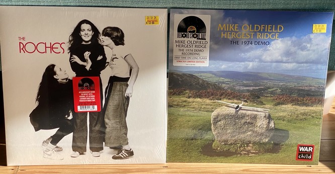 Two vinyl album covers side by side on a shelf: On the left, The Roches with three women in a black and white photo; on the right, Mike Oldfield's Hergest Ridge demo album with a landscape scene.
