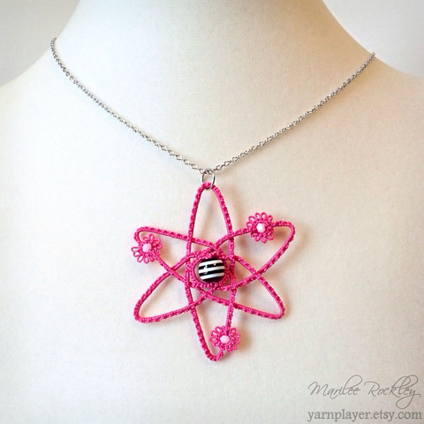 A handmade lace Rutherford model of an atom in tatting, with beads for the nucleus and electrons, made into a pendant necklace.