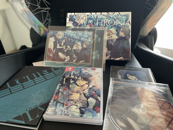 Presentation of the Utakata no Uchronia Limited Edition. Showing the standard game case featuring Yashiro & Hinagiku. To the left a game book with structured cover spelling “Uchronia” is presented. To the right of the game case lies a Drama CD and character cards, with their text covered by the CD. On top of the game case stands an acrylic standee and the limited edition box which feature the same art: The game’s main characters in street fashion. 